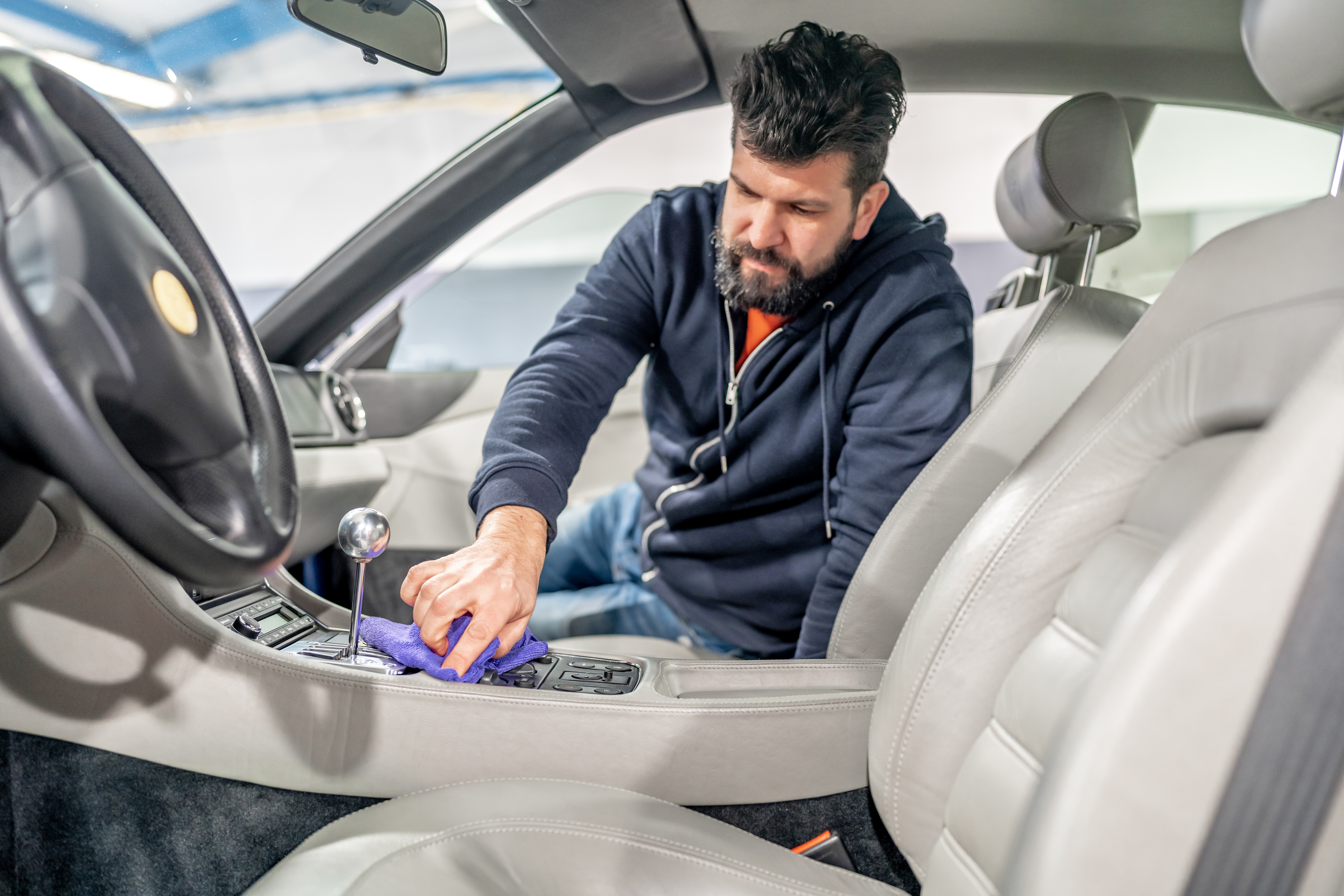 Technician hand-cleaning and polishing luxury car interior center console with microfiber cloth